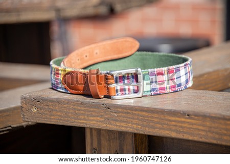 A madras pattern leather tab point belt in the sunlight outdoors.