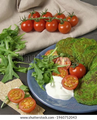spinach and zucchini pancakes lie on a beautiful blue plate, decorated with a cherry tomato sprig, which lie on a cotton napkin. on a dark background