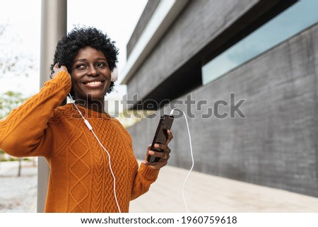 beautiful african woman listening to music with her smart phone and headphones on the street. Relaxed black girl using her cell phone as music player. Copy space