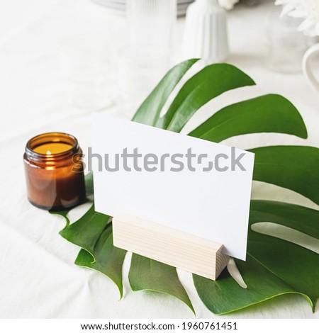 Mock up label the blank menu frame in bar restaurant, Stand for booklets with white paper, wooden tent card on monstera leaf on restaurant table