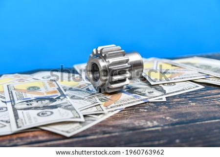 A gear wheel made on a gear cutting machine lies on dollar bills. The concept of advertising and selling industrial engineering services