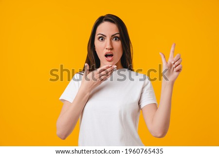 Surprised by sales, discounts and offers young caucasian woman pointing at copy space isolated over yellow background. Shocked latin-american woman showing advertisement place