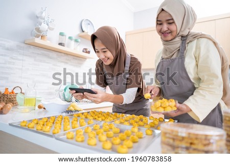 two muslim woman taking picture of the food product they made at home. small business muslim selling nastar cake for eid mubarak