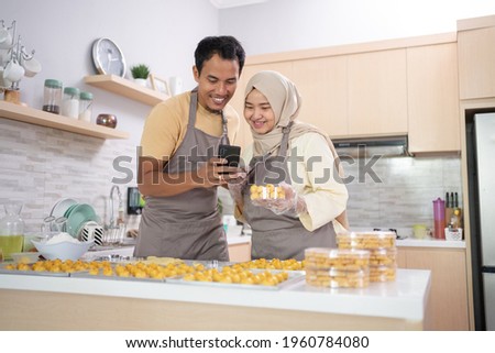 muslim couple use mobile phone to promote their product of snack for eid mubarak Royalty-Free Stock Photo #1960784080