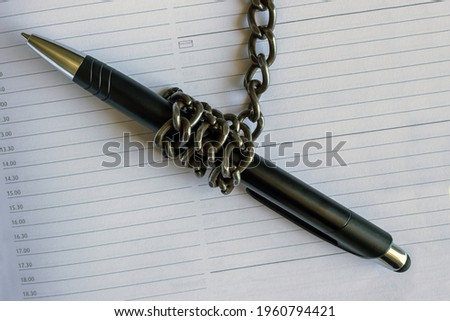 A pen wrapped in an iron chain lies on an empty notebook. Concept- restriction of freedom of speech. Royalty-Free Stock Photo #1960794421
