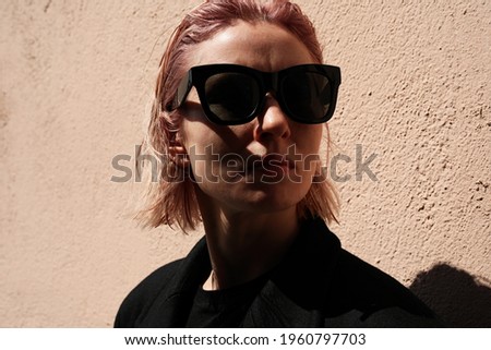 Headshot of young woman with pinkish hair, wearing sunglasses. Outdoor.