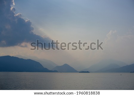 Blue yellow sunset on lake with storm cloud and misty mountains in background, diagonal ray of light