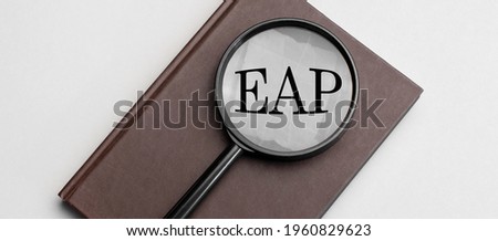 Magnifying glass with eap sign and brown notebook on grey background.