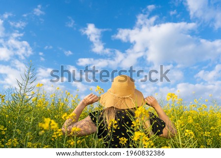 Woman holding sun hat in yellow flowers field at sunset.Happy female in spring sunny day concept lifestyle.