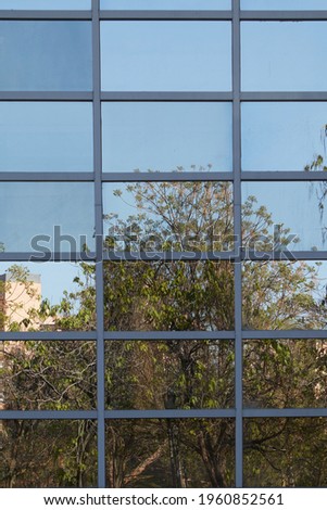 Glass building facade detail where the blue sky and some trees are reflected. Vertical photo.