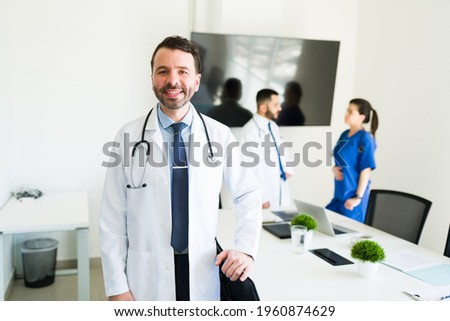 Portrait of a handsome hospital director in a white coat and a stethoscope smiling before starting a meeting with the medical board Royalty-Free Stock Photo #1960874629