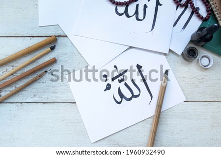Arabic handwriting with ink on paper, Arabic letters mean the name of Muslim god "Allah" wooden pen on table, handwriting Khat