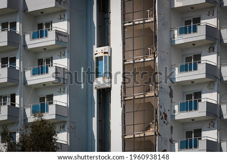 An old abandoned hotel building with broken glass, an elevator on the street, ripped air conditioners and signs in a tropical country with palm trees against a bright sky