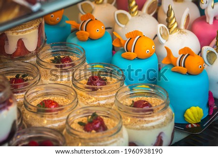 Close-up of creamy mousse cake in small jars decorated with strawberries and cake for children with fish and unicorns