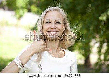 Portrait of attractive young woman on open air. Woman making a call me sign outdoors 