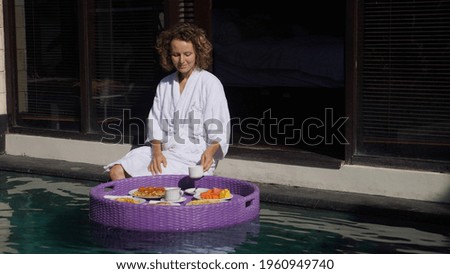 Floating breakfast concept. Morning of a blonde woman in a bathrobe in a luxurious resort. 