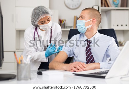 Medical nurse in safety gloves and protective mask making vaccine injection to a patient in health clinic Royalty-Free Stock Photo #1960992580