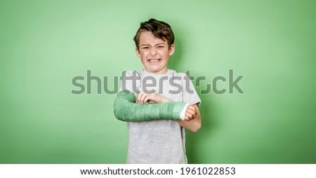 cool young schoolboy with broken arm and green arm plaster posing in front of green background Royalty-Free Stock Photo #1961022853