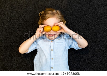 Happy boy, cover his eyes with painted eggs. Black background.