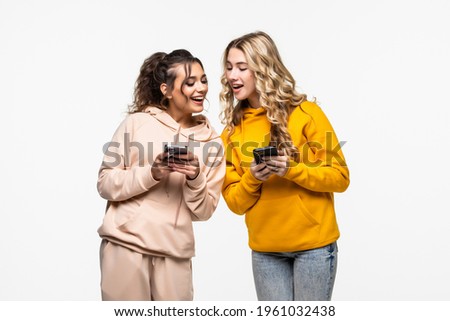 Two cheerful excited young women use smartphones over white background