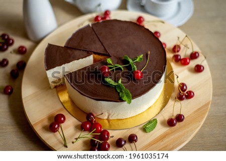 delicious Bird's Milk Cake with chocolate and cherry. Gold stand. On a wooden plank. on a grey background.