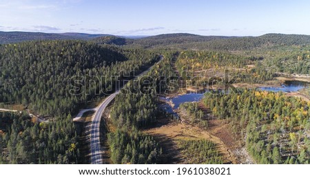 Aerial drone shot of road e75, surrounded by hills and foliage forest, sunny autumn day, in Inari, Lapland, Finland