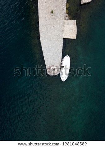 Drone photo. The boat is moored to lighthouse on artificial island – Our Lady of the Rocks near Perast in Kotor Bay, Montenegro. Minimalism aerial photography. Stone plateau. Dark blue Adriatic sea.