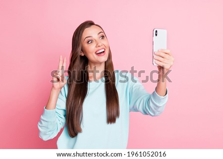 Photo of attractive charming young lady wear blue sweater hold phone show v-sign selfie isolated on pink color background