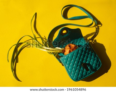 Vegetable shopping concept. Green onion in a green purse on yellow background. Vegetable in petrol blue woman bag. Layout with copy space. Grocery bag creative idea. Minimalist lifestyle