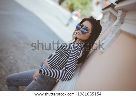 A Dutch angle shot of a cool, fashionable teenager with blue sunglasses leaning on an apartment wall Royalty-Free Stock Photo #1961055154