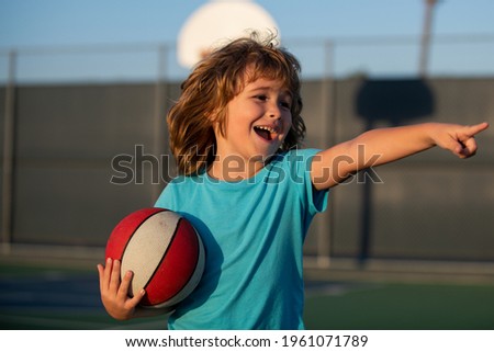 Happy smilin kid playing basketball, pointing showing gesture. Activity and sport for kids.
