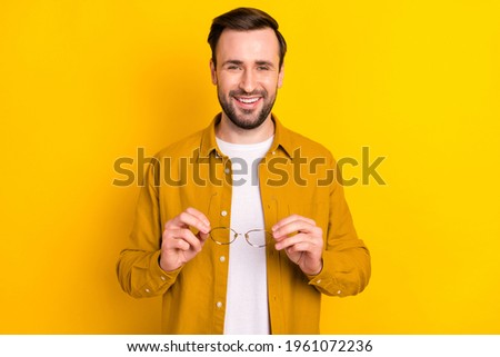 Photo of clever charming young guy wear casual clothes holding glasses smiling isolated yellow color background