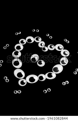 Puppet eyes of different sizes, laid out in the shape of a heart on a black background