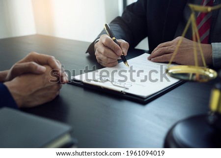 The lawyer is write drafting a legal document while listening to the client's information on the table with scale and gavel