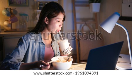 asian freelancer woman eats instant noodles and tapioca ball milk tea with laptop computer to work at home in the evening Royalty-Free Stock Photo #1961094391