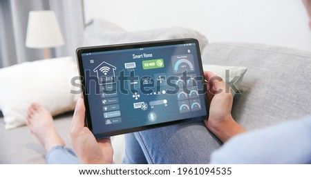 Iot Smart Home Concept - rear view of asian woman ask digital tablet to set temperature of air conditioner more higher by voice at home and all the electric meter in house getting energy-efficient