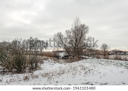 Simple wooden bridge in a snowy winter landscape. The photo was taken on a cloudy day in the Dutch province of North Brabant.