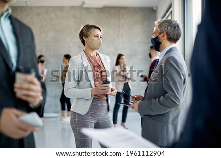 Businesswoman and her coworker wearing protective face masks and communicating after education event in a hallway of an office building. Royalty-Free Stock Photo #1961112904