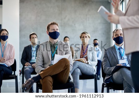 Male entrepreneur and his coworkers wearing face masks while listing to a presenter during business seminar in board room.