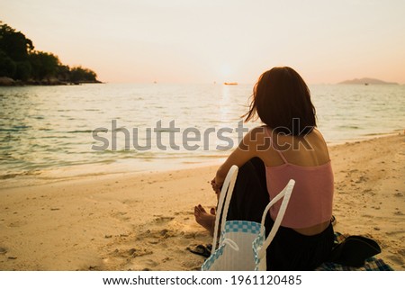 Asian woman sitting on the beach with looking at the sun on the sunset time. Travel and relax concept. picture looking Alone or sad. Copy space for text.