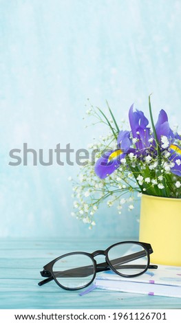 A bouquet of fresh irises in a mug, a book and glasses. Summer, vacation concept