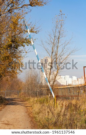 old rusty barrier blocks the road from the village to the city against the background of the sky and city buildings