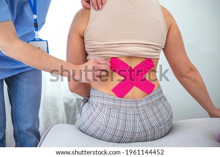 Close up shot of a female patient's lower back with kinesio tape. Kinesiology, physical therapy, rehabilitation concept. Cropped shot close up. Chiropractor applying three kinesiology tapes. 
