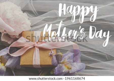 Happy mother's day. Happy mother's day text and peony and iris flowers and gift box on soft fabric on dark wood. Stylish floral greeting card. Handwritten lettering. Mothers day