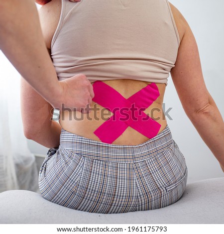 Chiropractor applying three kinesiology tapes. Chiropractor applying two kinesiology tapes to the back of a woman for pain relieve. Patient receives Kinesio Tape or Physio Tape for Back Pain 