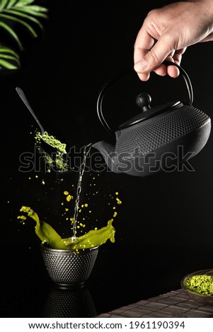 Water poured into a dark cup of matcha tea on a black background. Vertical format.