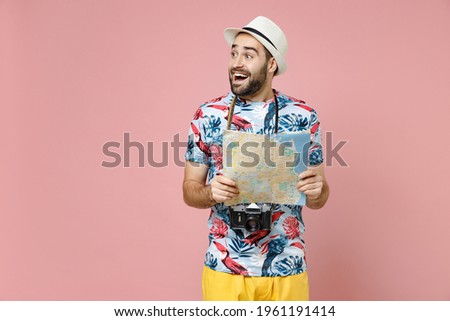 Excited young traveler tourist man in summer clothes hat hold city map looking aside isolated on pink background studio portrait. Passenger traveling abroad on weekends. Air flight journey concept
