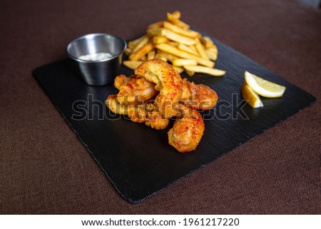 fish in batter with sauce and fries on a black plate.