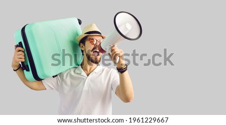Young caucasian tourist man in summer hat with luggage suitcase on shoulder screaming on megaphone advertising great tour agency offer, sale discount. Studio portrait with copy space Royalty-Free Stock Photo #1961229667