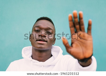 Portrait of young african black man against a green wall with white sweatshirt doing stop sign with is hand. Stop racism protest concept. BLM 